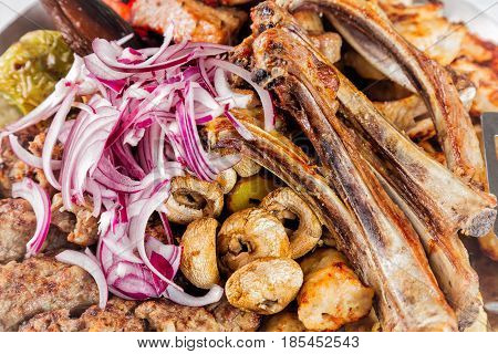 Meat plate with delicious pieces of meat ribs grilled potatoes and mushrooms with onion. Close up image with selective focus.