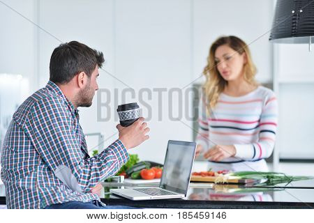 Couple standing and sitting at the kitchen while smiling and man reading a newspaper and holding mug before work