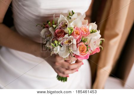 Bride and groom holding bridal bouquet close up. red and white roses, freesia, brunia decorated in composition.