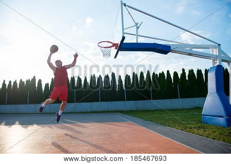 Young man jumping and making a fantastic slam dunk playing streetball, basketball. Urban authentic.