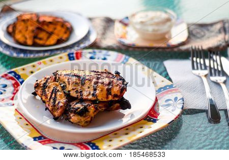 Grilled chicken on a plate with sweet potatoes and sauce in the background. These lean chicken breasts were marinated and cooked on the bbq (Barbecue). The perfect food for a healthy summer meal!