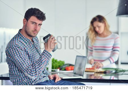 Couple standing and sitting at the kitchen while smiling and man reading a newspaper and holding mug before work