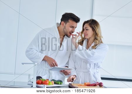 Couple in home kitchen using electronic tablet.
