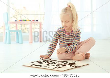 Cute little girl playing with letters while sitting on floor at home