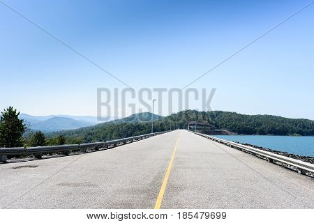 The crest road of Queen Sirikit Dam in Uttaradit Province Thailand in perspective view with blue sky