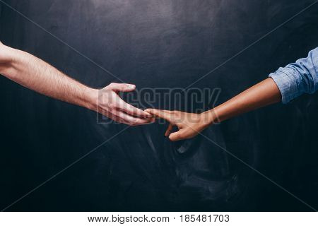 Reconnection of relationship or breakup.Two hands hold each other. Unrecognizable white guy and black woman on a dark background holding hands.