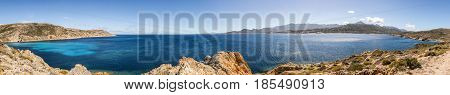 Panoramic view of Revellata lighthouse and west coast of Corsica looking across mediterranean sea towards the citadel of Calvi with snow capped mountains in the distance