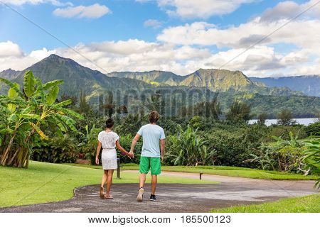 Couple tourists walking on Hawaii vacation. Two young people relaxing in Hanalei Bay resort in Kauai, Hawaii travel beach destination with Kauai mountains in the background.