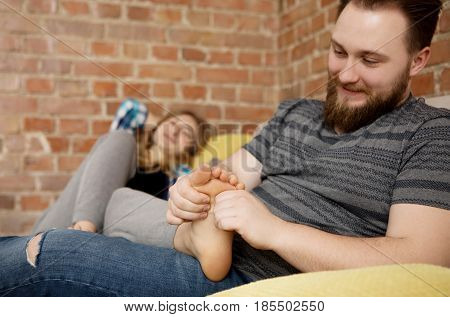 Two young people relaxing on sofa. Man massaging woman's feet.