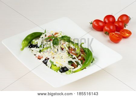 Traditional classic Shopska salad with tomatoes, peppers, cucumbers and cheese in white dish on white wooden table. Bulgarian cuisine, Balkan culture