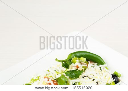 Traditional classic Shopska salad with tomatoes, peppers, cucumbers and cheese in white dish on white wooden table. Bulgarian cuisine, Balkan culture