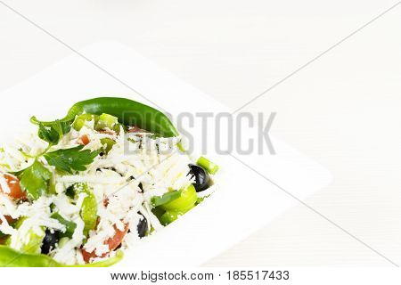 Traditional classic Shopska salad with tomatoes, peppers, cucumbers and cheese in white dish on white wooden table. Bulgarian cuisine, Balkan culture