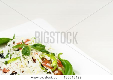 Traditional classic Shopska salad with tomatoes, peppers, cucumbers and cheese in white dish on white wooden table. Bulgarian cuisine, Balkan culture