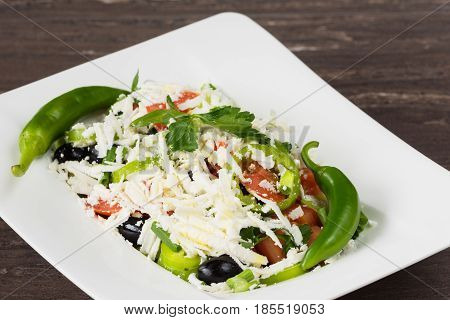 Traditional classic Shopska salad with tomatoes, peppers, cucumbers and cheese in white dish on grey wooden table. Bulgarian cuisine, Balkan culture