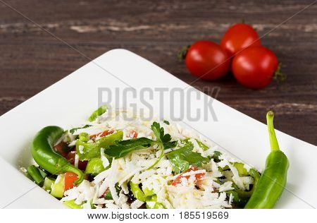 Traditional classic Shopska salad with tomatoes, peppers, cucumbers and cheese in white dish on grey wooden table. Bulgarian cuisine, Balkan culture