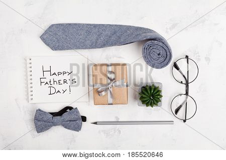 Happy Fathers Day background with notebook gift glasses necktie and bowtie on light working desk top view in flat lay style.
