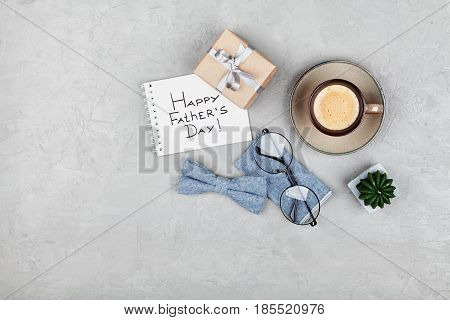 Happy Fathers Day background with morning coffee cup gift glasses and bowtie on stone gray desk top view in flat lay style.