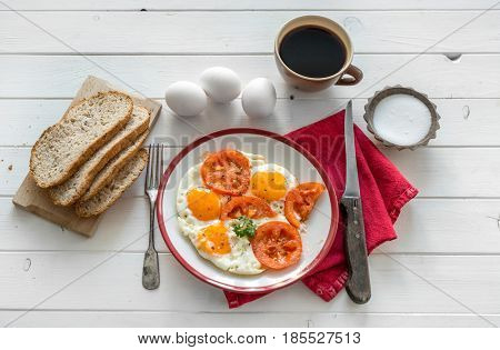Eggs fried overeasy served on white plate, tableware and red napkin, coffee on side