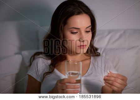 medicine, healthcare and people concept - woman with pill and glass of water in bed at night home