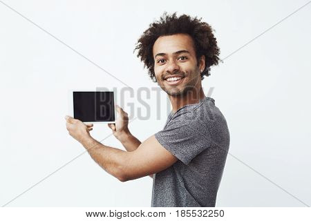 Cheerful african man smiling looking at camera showing tablet screen over white background. Copy space.