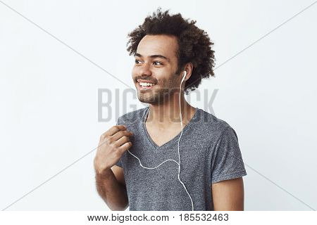 Young african man smiling putting out one headphone over white background. Copy space.
