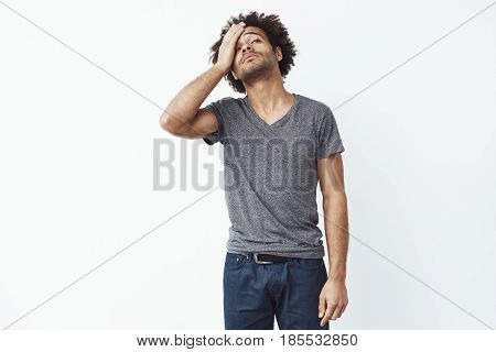 Upset and sad african man grabbing his forehead with hand standing missing the diversity lottery application deadline or forgetting to turn of electricity at home over white background. Copy space.