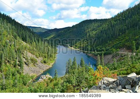 Between the hillock and the rock there is a mountain lake, a beautiful view of the forest and the taiga, the blue sky is the cessation of this lake
