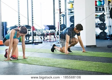 Runners in starting position. Young man and woman prepared for intense training session. Sports training in the gym.