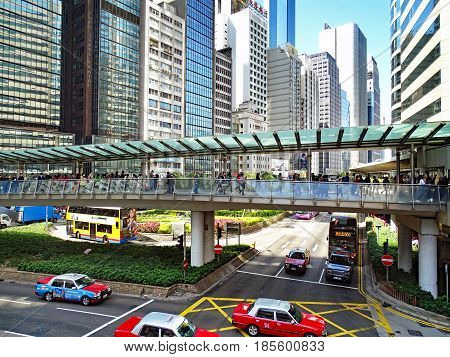 Central, Hong Kong - February 09, 2016: Traffic between high-rise buildings during the rush hour in the Central District on Hong Kong Island. Many people walk on a pedestrian bridge over a road crossing which is driven by cars and buses.