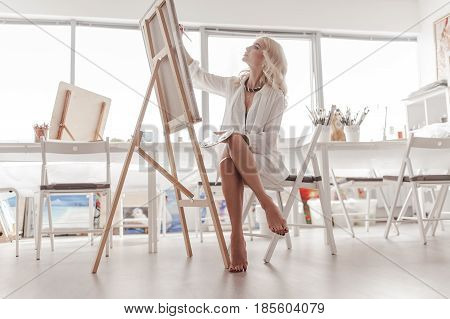 A woman paints a picture. The morning sun shines brightly in the window.