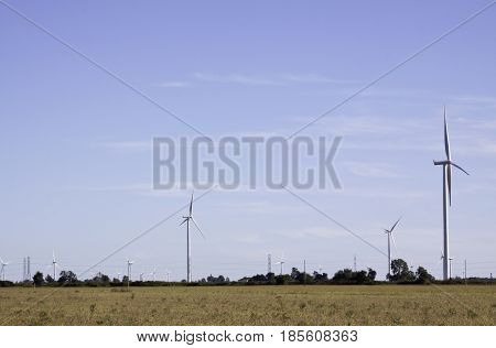 Close landscape view of multiple wind turbines in a farmer's field near Windsor, Ontario with the moon visible on a sunny late afternoon in September.