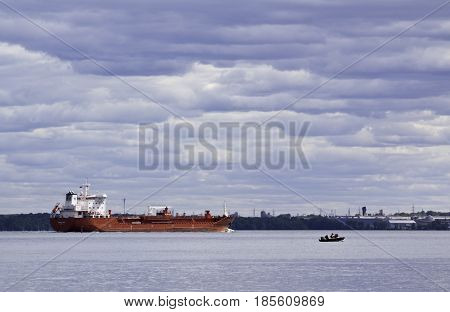 Notre Dame de Ile Perrot, Quebec - June 20, 2014 -- Wide landscape view of a very large red cargo ship and a very small boat motor boat in Lake St-Louis in Notre Dame de Ile Perrot, Quebec with trees foliage in the background on a sunny day in June.