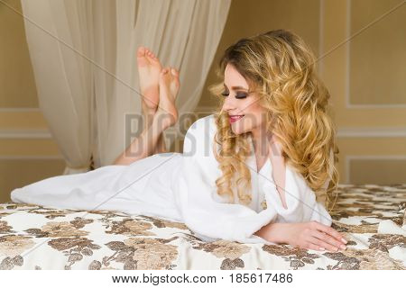 Beautiful seductive woman flirting with the camera lying on the bed with in White bathrobe looking up with a coquettish look.