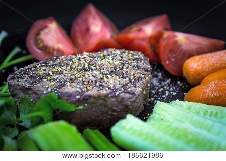 Delicious Chateaubriand beef steak on black plate with vegetables, close-up