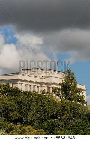 Auckland New Zealand - March 4 2017: War Memorial Museum building behind green vegetation and under rainy cloudy sky as seen from Parnell road.