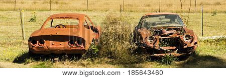 Two older cars sitting next to farmers barn that are rusting away.