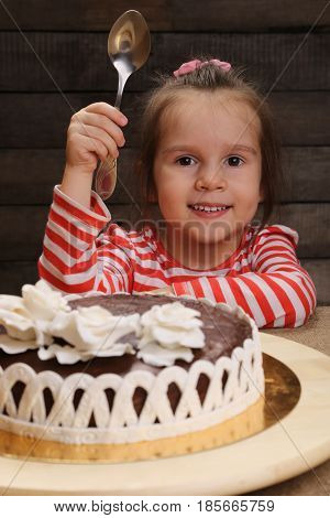 Cute excited smiling little girl with spoon in hand going to eat chocolate cake. The joys of childhood. Celebration party.