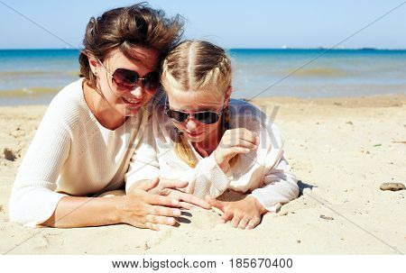 Daughter and her mom playing with sand on the beach