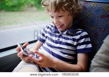 A small passenger of a city bus with a smartphone in hand. The boy looks at the smartphone screen and cheerfully smiles.