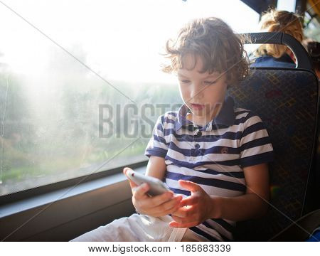 A small passenger of a city bus with a smartphone in hand. The boy sits at the window and looks with interest at the screen of the smartphone.