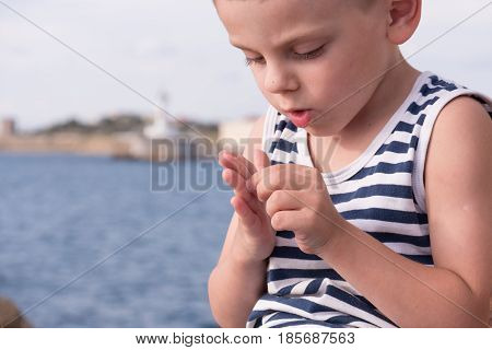 Attentive little boy wearing sailor stripes shirt gets a splinter from his finger