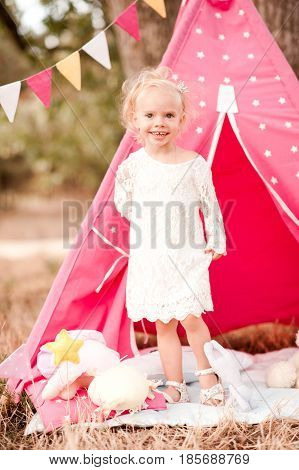 Smiling baby girl 3-4 year old playing in meadow outdoors. Wearing stylish white dress. Childhood. Summer time.