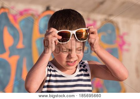 Little boy with white sunglasses with ocean sunset reflections squinted from the bright sun