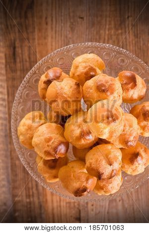 Sweet cream puffs in glass tray on wooden table.