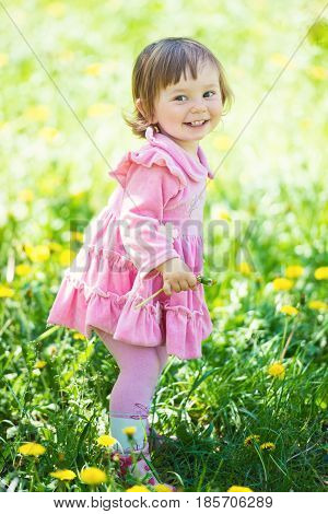 A little girl in a pink dress is laughing in a clearing with dandelions