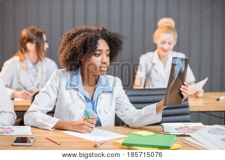 Multi ethnic group of medical students in uniform working on medical research sitting at the desk with x-ray and books in the modern classroom