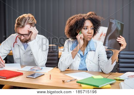 Multi ethnic group of medical students in uniform working on medical research sitting at the desk with x-ray and books in the modern classroom