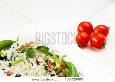Traditional classic Shopska salad with tomatoes, peppers, cucumbers and cheese in white dish on white wooden table. Bulgarian cuisine, Balkan culture