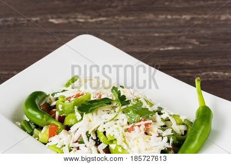 Traditional classic Shopska salad with tomatoes, peppers, cucumbers and cheese in white dish on grey wooden table. Bulgarian cuisine, Balkan culture