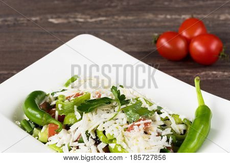 Traditional classic Shopska salad with tomatoes, peppers, cucumbers and cheese in white dish on grey wooden table. Bulgarian cuisine, Balkan culture